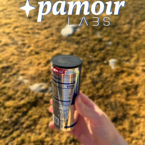 May include: A silver can with a black top and blue and white text. The can is labeled "160" and "Nutrition Facts". The can is being held by a hand in front of a blurry background of brown grass.