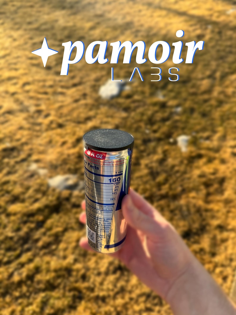May include: A silver can with a black top and blue and white text. The can is labeled "160" and "Nutrition Facts". The can is being held by a hand in front of a blurry background of brown grass.