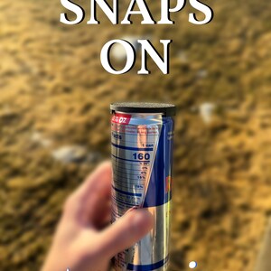 May include: A silver and blue Red Bull energy drink can with a black lid, held in a hand. The can's label displays nutritional facts. The words "SNAPS ON" are above the can, and the text "+pamoir LABS" is below.