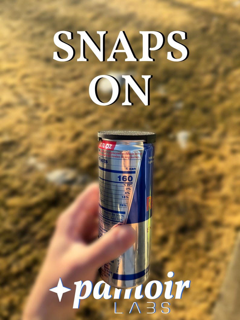 May include: A silver and blue Red Bull energy drink can with a black lid, held in a hand. The can's label displays nutritional facts. The words "SNAPS ON" are above the can, and the text "+pamoir LABS" is below.