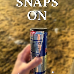 May include: A silver can with a black top and a nutrition facts label. The can is being held by a hand. The text "SNAPS ON" is written in white letters on a blurred background. The text "pamoir LABS" is written in white letters on a black star.