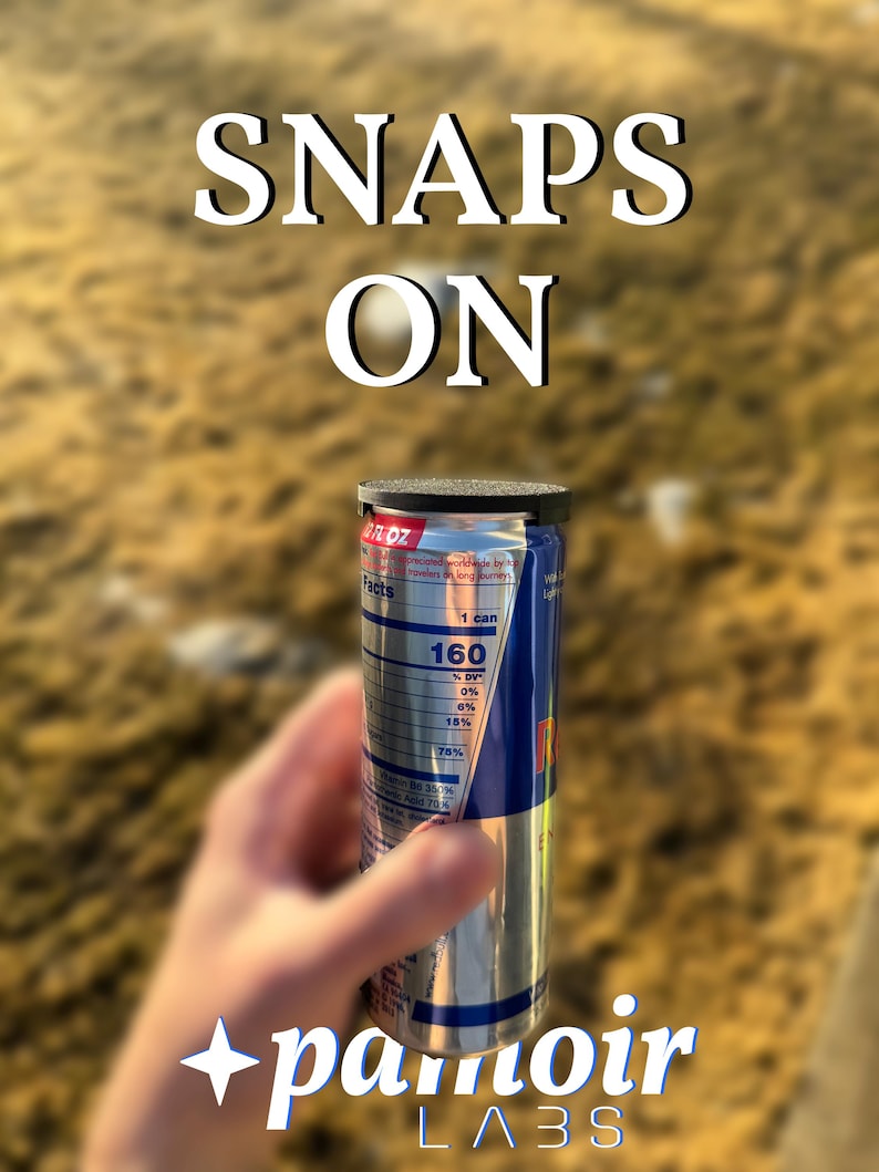 May include: A silver can with a black top and a nutrition facts label. The can is being held by a hand. The text "SNAPS ON" is written in white letters on a blurred background. The text "pamoir LABS" is written in white letters on a black star.