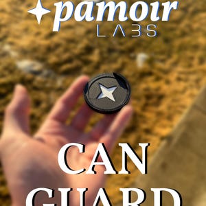 May include: A black can guard with a white star design in the center. The text "pamoir LABS" is at the top, and the words "CAN GUARD" are at the bottom. The background is blurred, with a natural, outdoor setting.
