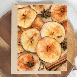 May include: A rectangular greeting card featuring a high-resolution print of dried apple slices, whole star anise, and cinnamon sticks. The composition displays a warm, golden-brown color palette with detailed textures of the fruit and spices.