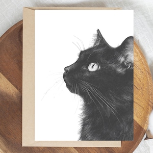 May include: A monochrome art print featuring a black cat in profile. The cat's fur is detailed, and its eye is open. The print is on a white background, with a brown card and wooden tray in the background.