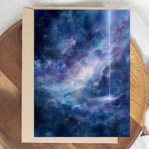 May include: Greeting card featuring a watercolor painting of a nebula in shades of blue, purple, and white. A bright vertical streak of light and a horizontal line add detail to the cosmic scene. The card is set in a brown envelope.