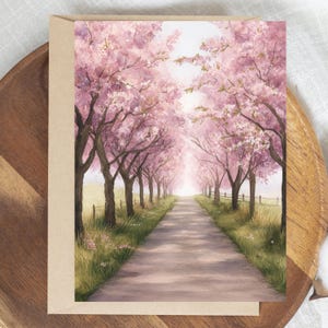 May include: A greeting card featuring a watercolor painting of a path lined with cherry blossom trees. The trees have pink flowers and brown trunks. The path leads to a bright, light-filled area. The card is set on a wooden tray.