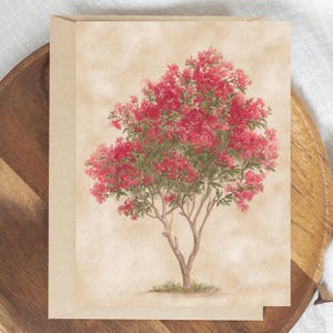 May include: A watercolor greeting card featuring a vibrant tree with red flowers and green foliage. The tree is set against a beige background, with a brown wooden tray in the background.
