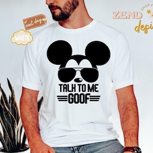 Puede incluir: Una camiseta blanca de manga corta con un gr&aacute;fico negro de la silueta de un rat&oacute;n con gafas de sol. Debajo del gr&aacute;fico, el texto dice TALK TO ME GOOF en letras may&uacute;sculas negras, flanqueado por l&iacute;neas horizontales a ambos lados de la palabra.