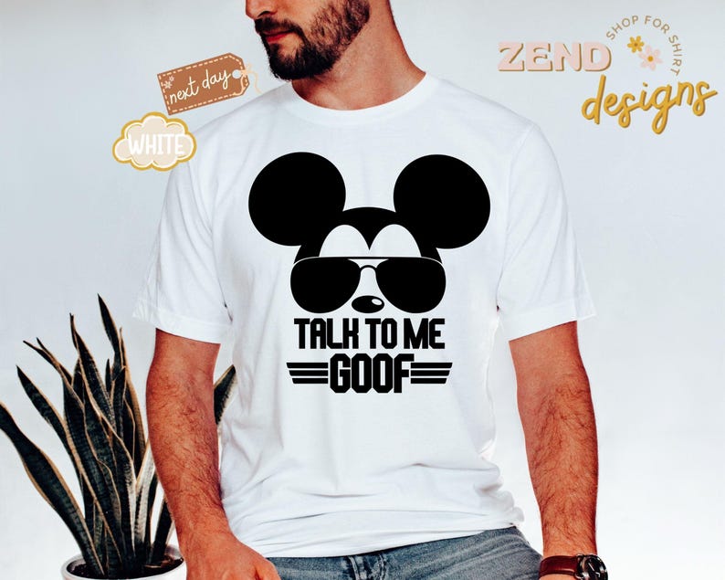 Puede incluir: Una camiseta blanca de manga corta con un gr&aacute;fico negro de la silueta de un rat&oacute;n con gafas de sol. Debajo del gr&aacute;fico, el texto dice TALK TO ME GOOF en letras may&uacute;sculas negras, flanqueado por l&iacute;neas horizontales a ambos lados de la palabra.