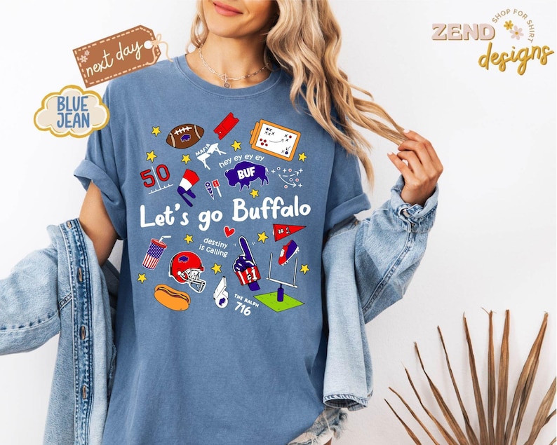 May include: A blue t-shirt with the text "Let's go Buffalo" and various graphics, including a football, helmet, and the number 50. The shirt has rolled-up sleeves and is worn with a denim jacket.