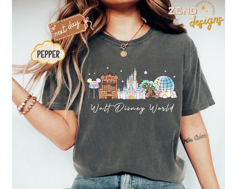 May include: Dark gray t-shirt featuring a colorful illustration of Walt Disney World landmarks. The design includes the Tower of Terror, Cinderella Castle, and Spaceship Earth, with the words "Walt Disney World" below.