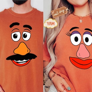 Könnte beinhalten: Zwei orangefarbene T-Shirts mit Cartoon-Gesichtern. Eines hat einen schwarzen Schnurrbart, eine orangefarbene Nase und einen lächelnden Mund. Das andere hat eine rosa Nase, rote Lippen und Wimpern. Die Shirts sind ein passendes Set.