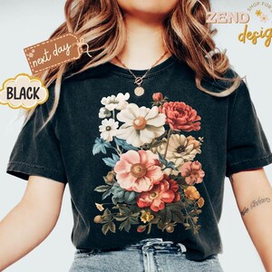 Puede incluir: Camiseta negra con un dise&ntilde;o de ramo floral en tonos rosa, rojo, blanco y amarillo. La camiseta tiene el texto "ZEND designs" y "next day". La camiseta es de cuello redondo y est&aacute; hecha de un material suave.