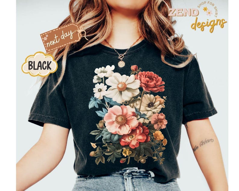 Puede incluir: Camiseta negra con un dise&ntilde;o de ramo floral en tonos rosa, rojo, blanco y amarillo. La camiseta tiene el texto "ZEND designs" y "next day". La camiseta es de cuello redondo y est&aacute; hecha de un material suave.