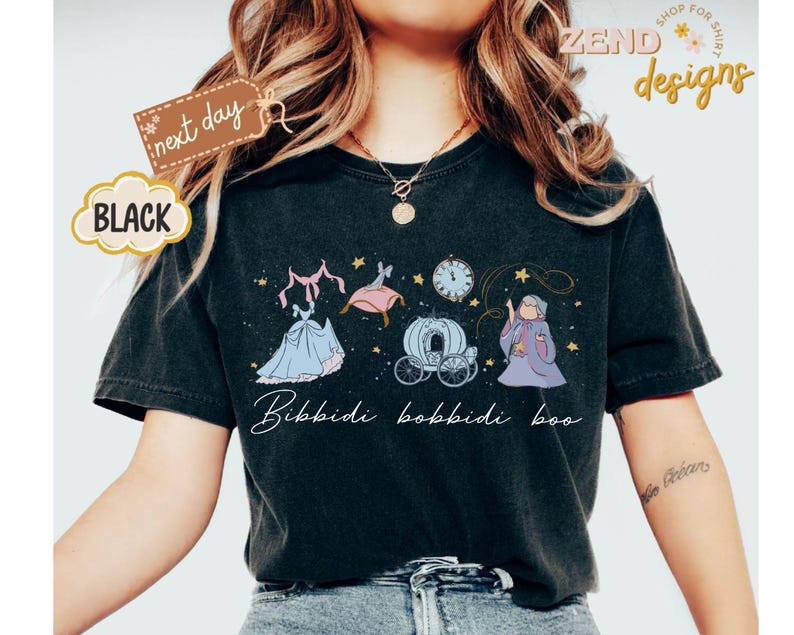 May include: Black t-shirt featuring a whimsical illustration of a fairytale scene with a dress, carriage, clock, and fairy godmother. The text "Bibbidi Bobbidi Boo" is written in a script font. The shirt has a vintage, worn look.