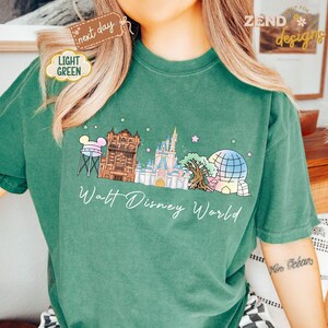 May include: A light green t-shirt featuring a colorful illustration of Walt Disney World landmarks, including Cinderella's castle and Spaceship Earth. The words "Walt Disney World" are written in a cursive font below the illustration.