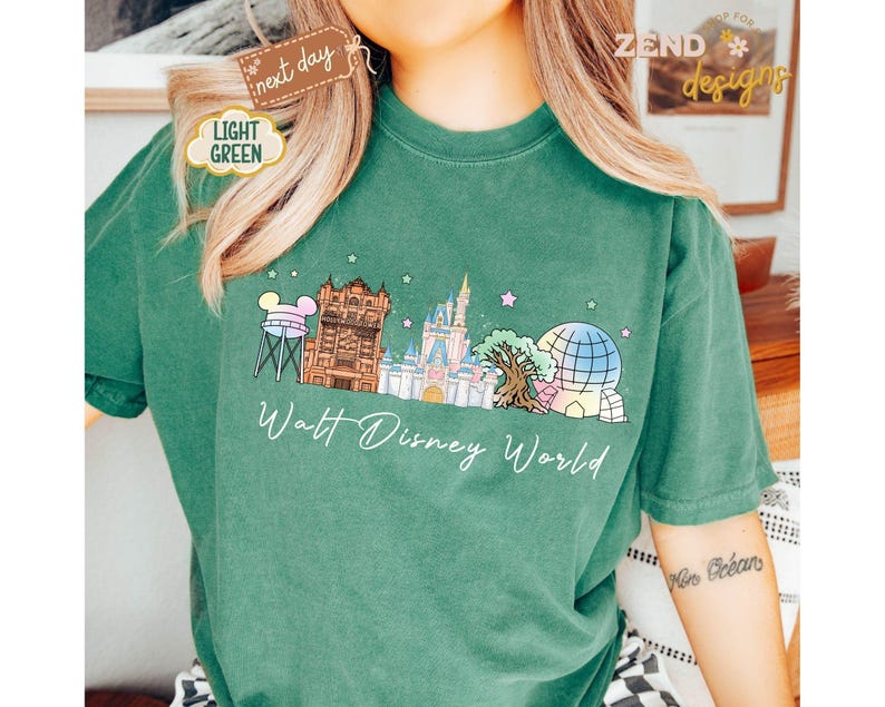May include: A light green t-shirt featuring a colorful illustration of Walt Disney World landmarks, including Cinderella's castle and Spaceship Earth. The words "Walt Disney World" are written in a cursive font below the illustration.