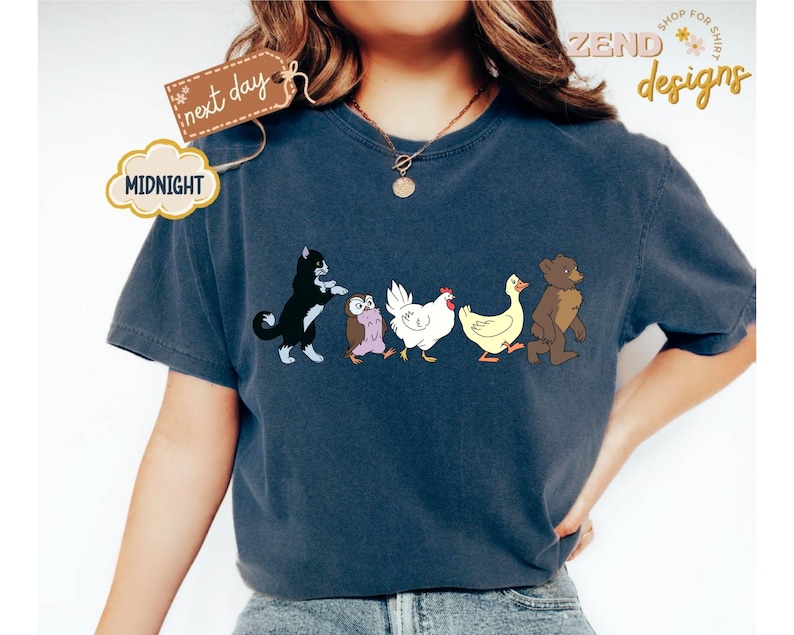 May include: Navy blue t-shirt featuring a whimsical illustration of a black and white cat, an owl, a white chicken, a yellow duck, and a brown bear walking together. The shirt has the text "ZEND designs" and "Midnight" on it.
