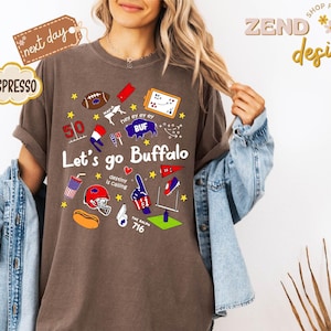 May include: Espresso-colored t-shirt with the text "Let's go Buffalo" and various sports-themed graphics. The design includes a football, a helmet, and the number 50. The shirt also has the text "destiny is calling".