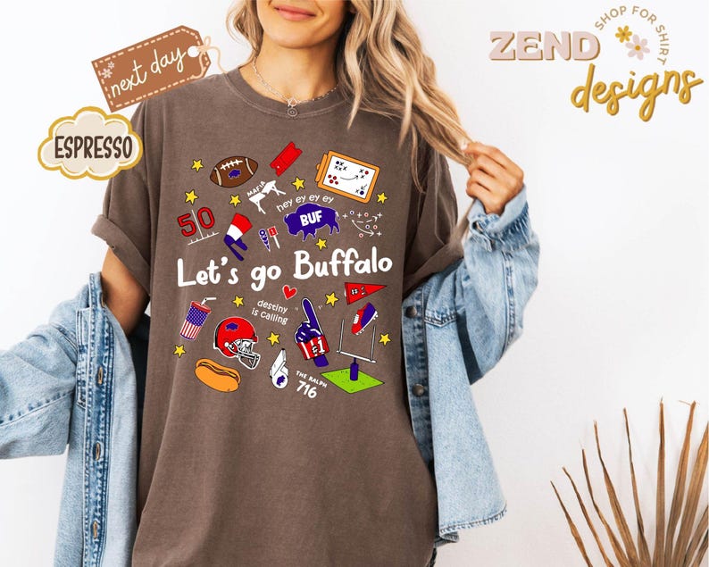 May include: Espresso-colored t-shirt with the text "Let's go Buffalo" and various sports-themed graphics. The design includes a football, a helmet, and the number 50. The shirt also has the text "destiny is calling".