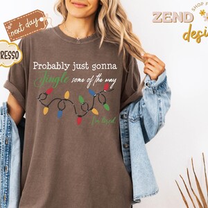 Pode incluir: Camiseta cor espresso com o texto "Probably just gonna Jingle some of the way" e uma sequ&ecirc;ncia de luzes de Natal coloridas. A camiseta tamb&eacute;m tem o texto "I'm tired". A camiseta faz parte da cole&ccedil;&atilde;o "Zend designs".