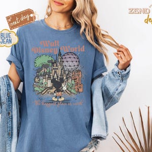 以下が含まれることがあります： ウォルト・ディズニー・ワールドのグラフィックがプリントされた青いTシャツ。お城、スペースシップ・アース、ミッキーマウスが描かれています。「Walt Disney World」と「The happiest place on earth」の文字がプリントされています。ヴィンテージ風のTシャツです。