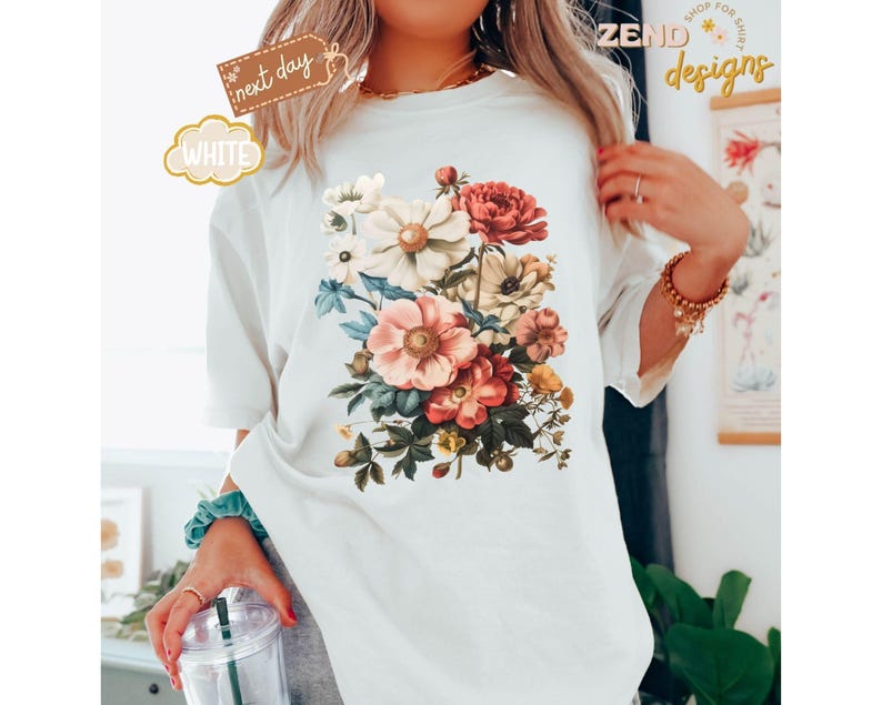Puede incluir: Camiseta blanca con un dise&ntilde;o de ramo floral vintage en tonos rosa, rojo y crema. La camiseta tiene cuello redondo y mangas cortas. Las palabras "next day" y "white" est&aacute;n impresas en la camiseta.
