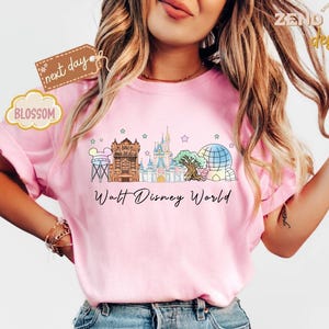 May include: Pink t-shirt with a colorful graphic of Walt Disney World landmarks, including the Tower of Terror, Cinderella Castle, and Spaceship Earth. The words "Walt Disney World" are printed below the graphic.