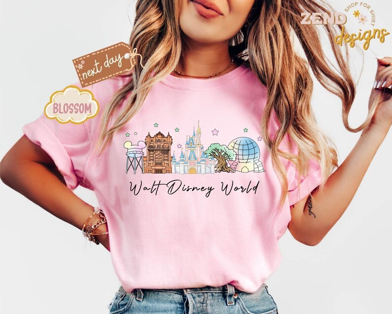 May include: Pink t-shirt with a colorful graphic of Walt Disney World landmarks, including the Tower of Terror, Cinderella Castle, and Spaceship Earth. The words "Walt Disney World" are printed below the graphic.