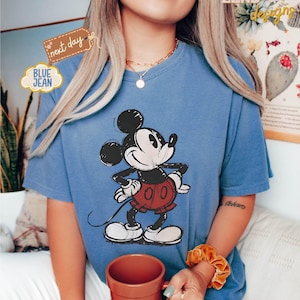 May include: A blue t-shirt with a black and white cartoon image of Mickey Mouse. Mickey Mouse is wearing red shorts with white polka dots. The t-shirt has a distressed look.