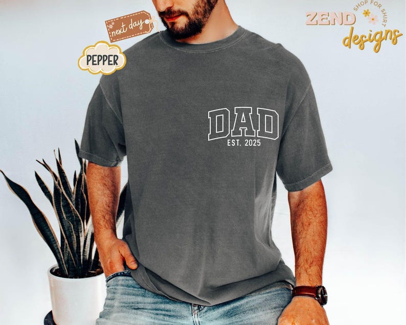 May include: A charcoal gray t-shirt with a white graphic that says "DAD EST. 2025".