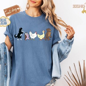 May include: Blue jean t-shirt featuring a line of cartoon animals: a black and white cat, an owl, a white chicken, a yellow duck, and a brown bear. The shirt has the text "next day" and "BLUE JEAN" on it. The shirt is from "ZEND designs".