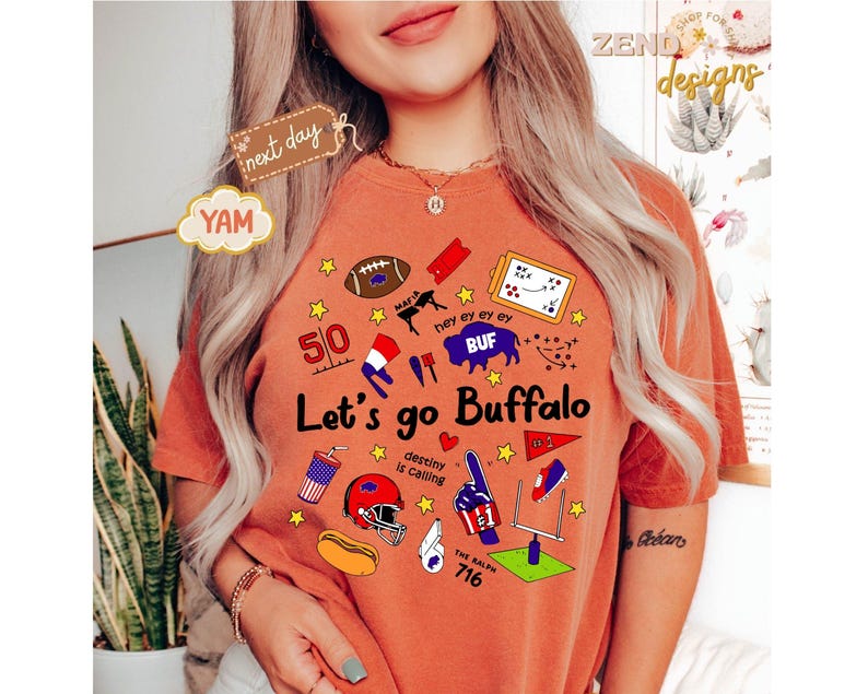 May include: Burnt orange t-shirt with the text "Let's go Buffalo" and various sports-themed graphics, including a football, helmet, and goalpost. The shirt also features the text "destiny is calling" and "The Ralph 716".