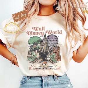 以下が含まれることがあります： ウォルト・ディズニー・ワールドのヴィンテージスタイルのイラストが描かれたアイボリー色のTシャツ。デザインにはお城、スペースシップ・アース、ミッキーマウスが含まれています。「ウォルト・ディズニー・ワールド」と「地球上で最も幸せな場所」と書かれています。
