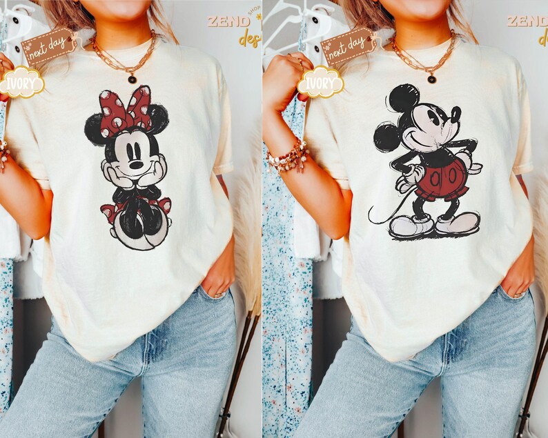 May include: Two women wearing cream-colored t-shirts with cartoon images of Mickey Mouse and Minnie Mouse. The shirts have a distressed look and the images are in black and white with red accents.