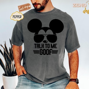Puede incluir: Una camiseta de manga corta gris carb&oacute;n con un gr&aacute;fico negro de la silueta de un rat&oacute;n con gafas de sol. Debajo del gr&aacute;fico, el texto dice TALK TO ME GOOF en letras may&uacute;sculas negras en negrita con l&iacute;neas horizontales a ambos lados de GOOF.
