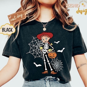 K&ouml;nnte beinhalten: Schwarzes T-Shirt mit einem Halloween-Motiv. Das Design zeigt ein Cartoon-Skelett, das als Cowgirl verkleidet ist und einen K&uuml;rbis-Eimer h&auml;lt, mit Spinnweben und Flederm&auml;usen. Das Shirt hat den Text "next day" und "BLACK".