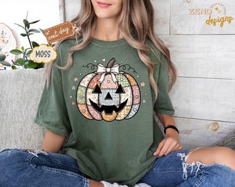 May include: Green t-shirt featuring a patchwork pumpkin design with a smiling jack-o'-lantern face, a white bow, and floral accents. The shirt has short sleeves and a relaxed fit. The text "next day" and "MOSS" are visible on the left side of the image. The text "ZEND designs" is visible on the right side.