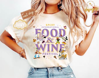 May include: Ivory-colored t-shirt featuring the text "EPCOT INTERNATIONAL FOOD & WINE FESTIVAL" in purple. The shirt has cartoon characters like Mickey Mouse, Minnie Mouse, and Donald Duck. The shirt also has the text "next day" and "IVORY".