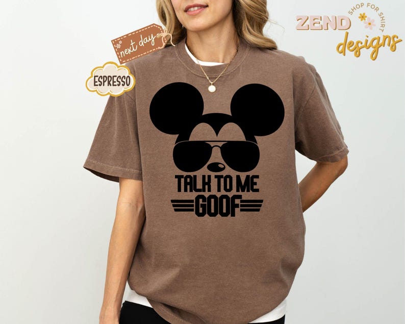 Puede incluir: Una camiseta marr&oacute;n de manga corta con un gr&aacute;fico negro de la silueta de un rat&oacute;n con gafas de sol. Debajo del gr&aacute;fico, el texto "TALK TO ME GOOF" aparece en letras may&uacute;sculas negras, flanqueado por dos l&iacute;neas horizontales a cada lado de GOOF.