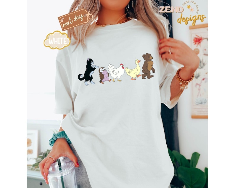 May include: White t-shirt featuring a line of cartoon animals: a black cat, an owl, a chicken, a duck, and a bear. The shirt has the word "WHITE" in a bubble and a tag that says "next day".