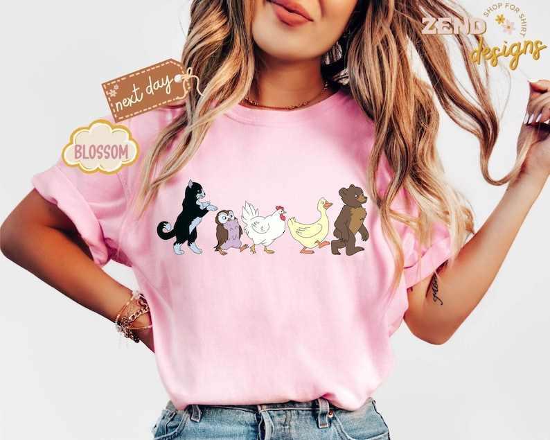 May include: Pink t-shirt featuring a line of cartoon animals: a black cat, an owl, a chicken, a duck, and a bear. The shirt has the text "next day" and "BLOSSOM" on it. The shirt is from "ZEND designs".