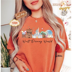 May include: Burnt orange t-shirt featuring a colorful illustration of the Walt Disney World skyline. The design includes iconic landmarks like Cinderella's Castle and Spaceship Earth, with the words "Walt Disney World" in a script font.