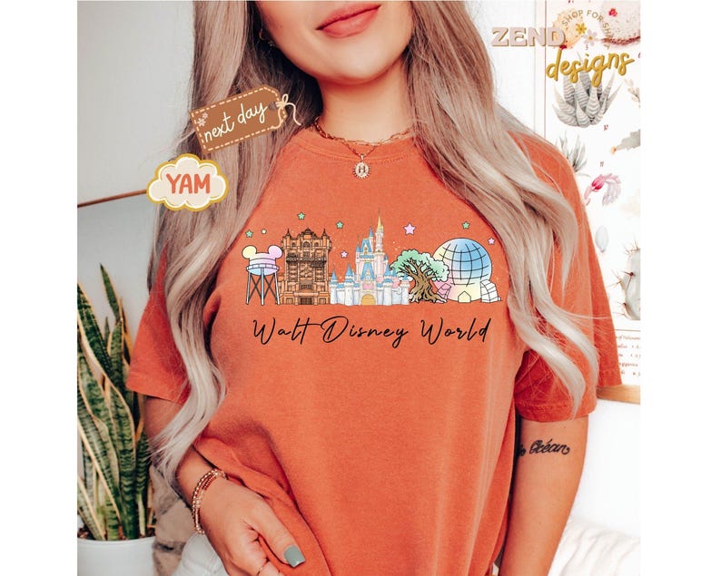 May include: Burnt orange t-shirt featuring a colorful illustration of the Walt Disney World skyline. The design includes iconic landmarks like Cinderella's Castle and Spaceship Earth, with the words "Walt Disney World" in a script font.
