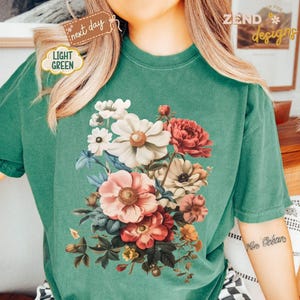 Puede incluir: Camiseta verde claro con un dise&ntilde;o de ramo floral en tonos rosas, rojos, blancos y amarillos. La camiseta tiene un corte holgado y mangas cortas. El texto "ZEND designs" es visible.