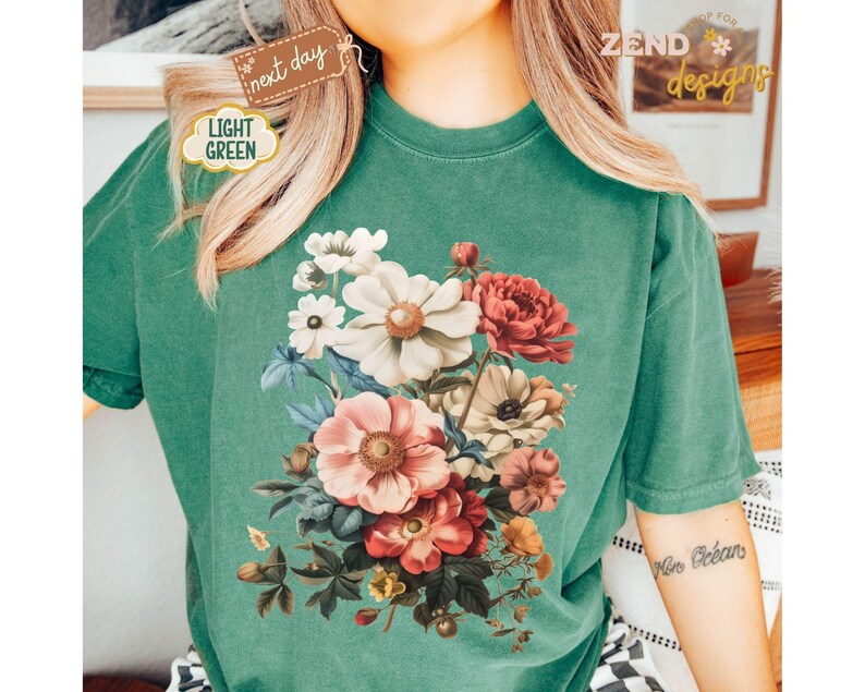 Puede incluir: Camiseta verde claro con un dise&ntilde;o de ramo floral en tonos rosas, rojos, blancos y amarillos. La camiseta tiene un corte holgado y mangas cortas. El texto "ZEND designs" es visible.