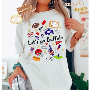 May include: White t-shirt with a colorful graphic design featuring the text "Let's go Buffalo" and various sports-themed illustrations. The design includes a football, helmet, and the number 716.