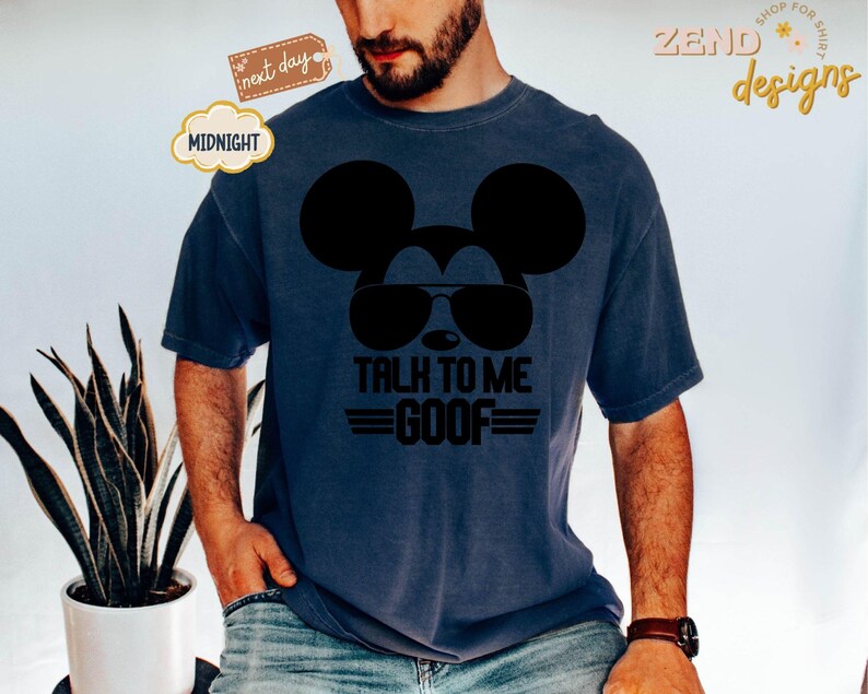 Puede incluir: Una camiseta de manga corta azul oscuro con un gr&aacute;fico negro de la silueta de un rat&oacute;n con gafas de aviador. Debajo del gr&aacute;fico, el texto dice TALK TO ME GOOF en letras may&uacute;sculas negras en negrita con l&iacute;neas horizontales a los lados.