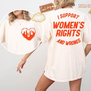 May include: A white t-shirt with the text "I support women's rights and wrongs" printed in orange on the back. The front of the shirt features a red heart with flames inside, surrounded by barbed wire.